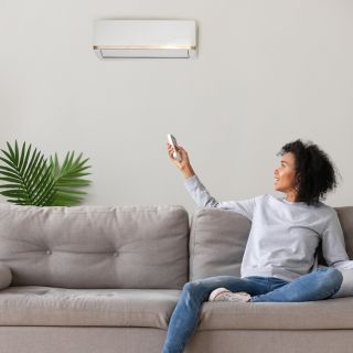 Donna sul divano regola condizionatore con telecomando, comfort domestico e risparmio energetico in estate