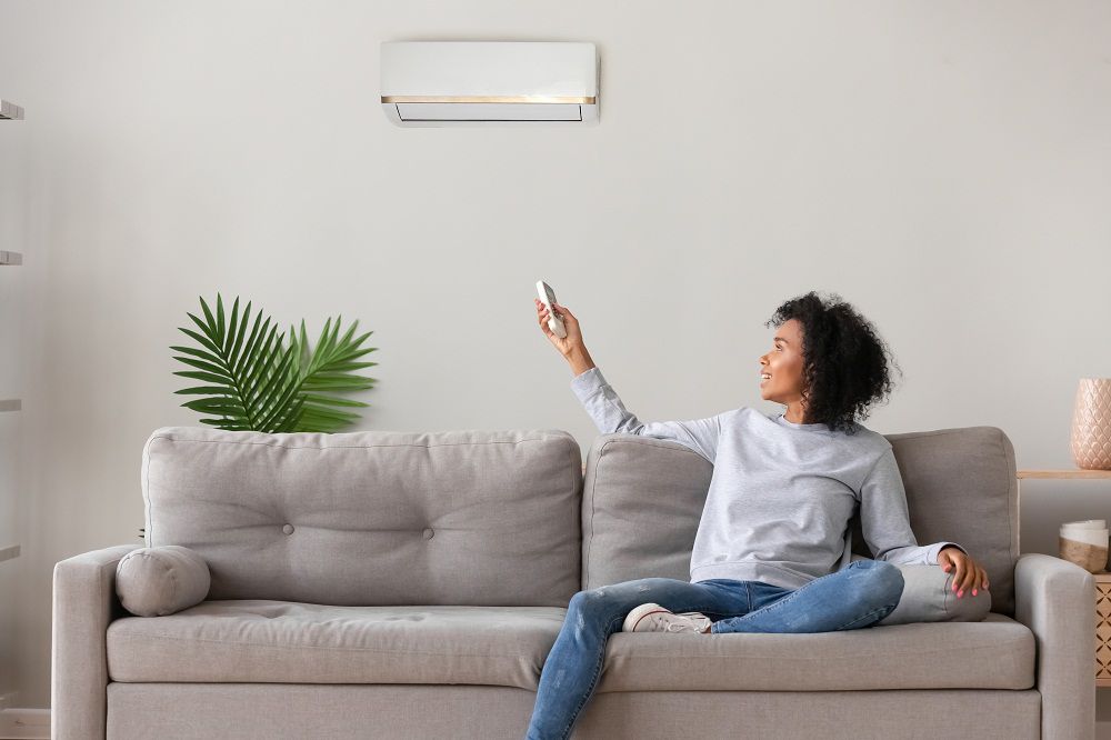 Donna sul divano regola condizionatore con telecomando, comfort domestico e risparmio energetico in estate