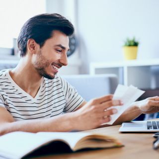 Uomo sorride mentre controlla bollette luce e gas al computer, concetto aumento prezzi energia autunno