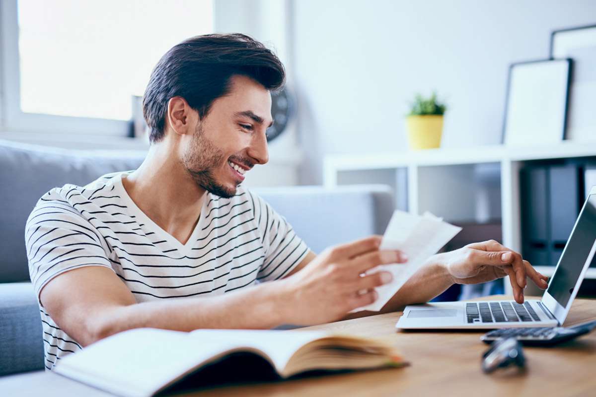 Uomo sorride mentre controlla bollette luce e gas al computer, concetto aumento prezzi energia autunno