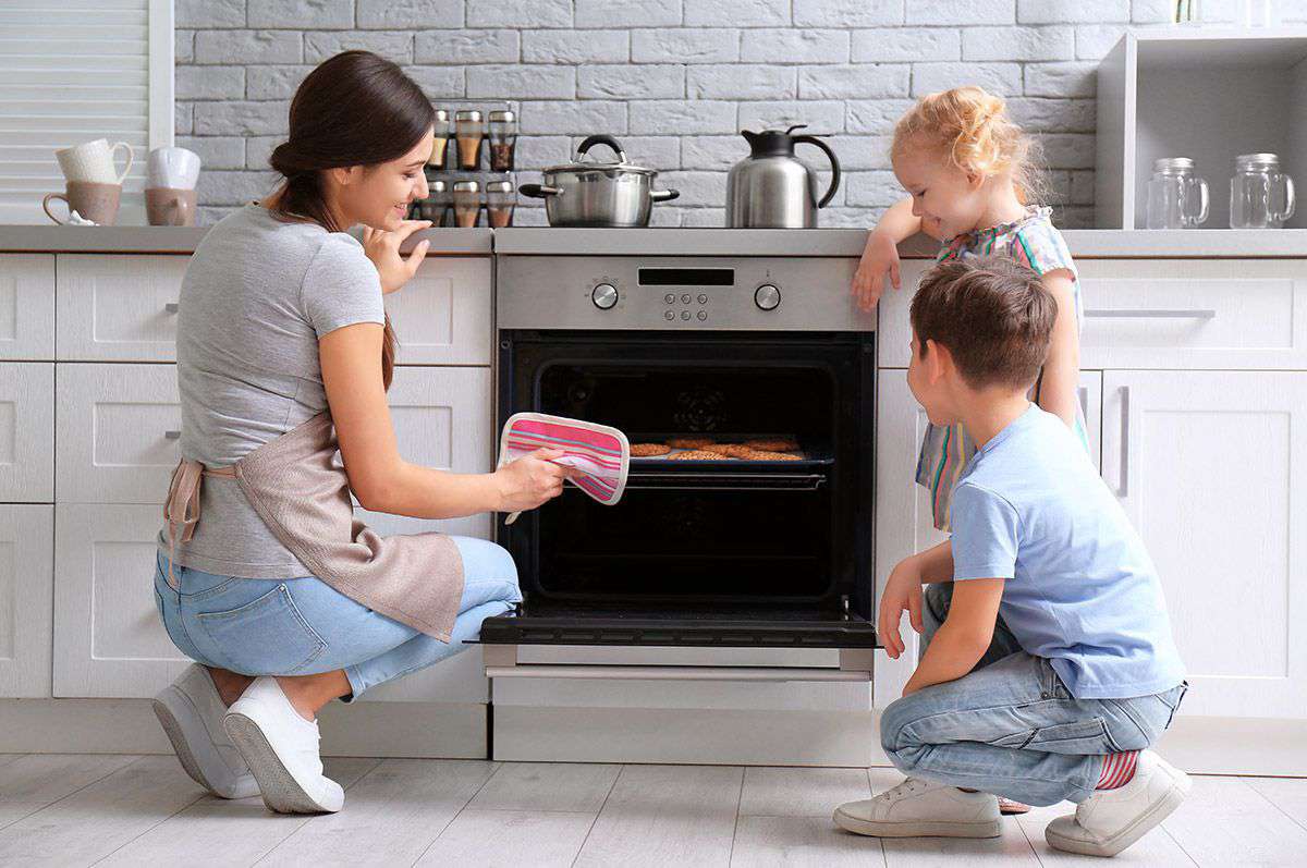 Mamma cucina biscotti con due bambini in cucina moderna, concetto di risparmio energetico e comfort domestico