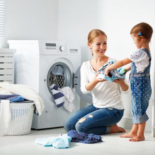 Mamma e bambina sorridenti fanno il bucato insieme in lavanderia moderna, risparmio energetico domestico