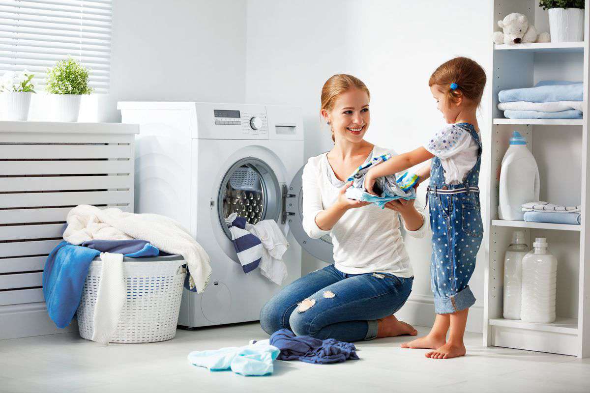 Mamma e bambina sorridenti fanno il bucato insieme in lavanderia moderna, risparmio energetico domestico