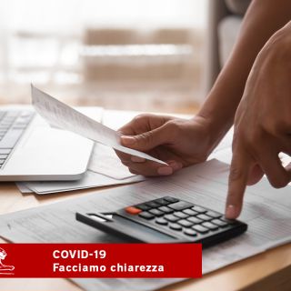 Mano che calcola bollette con calcolatrice e laptop, informazioni su rateizzazione e rinvii pagamenti COVID-19