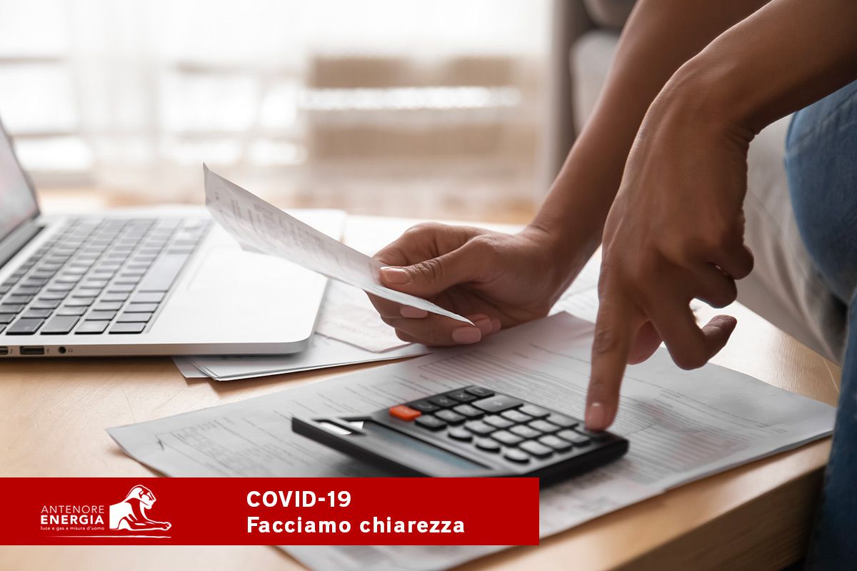 Mano che calcola bollette con calcolatrice e laptop, informazioni su rateizzazione e rinvii pagamenti COVID-19