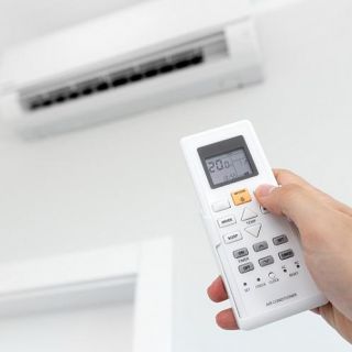 Telecomando condizionatore impostato a 26 gradi, dettaglio mano che regola temperatura per risparmio bolletta energetica