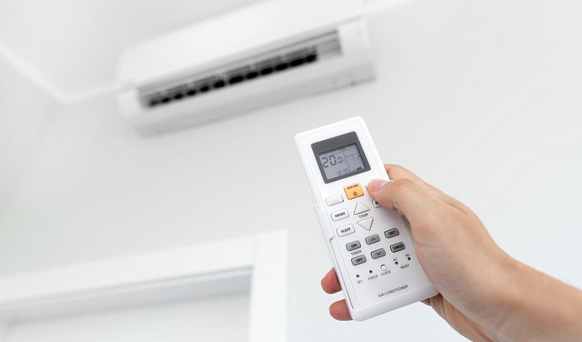 Telecomando condizionatore impostato a 26 gradi, dettaglio mano che regola temperatura per risparmio bolletta energetica