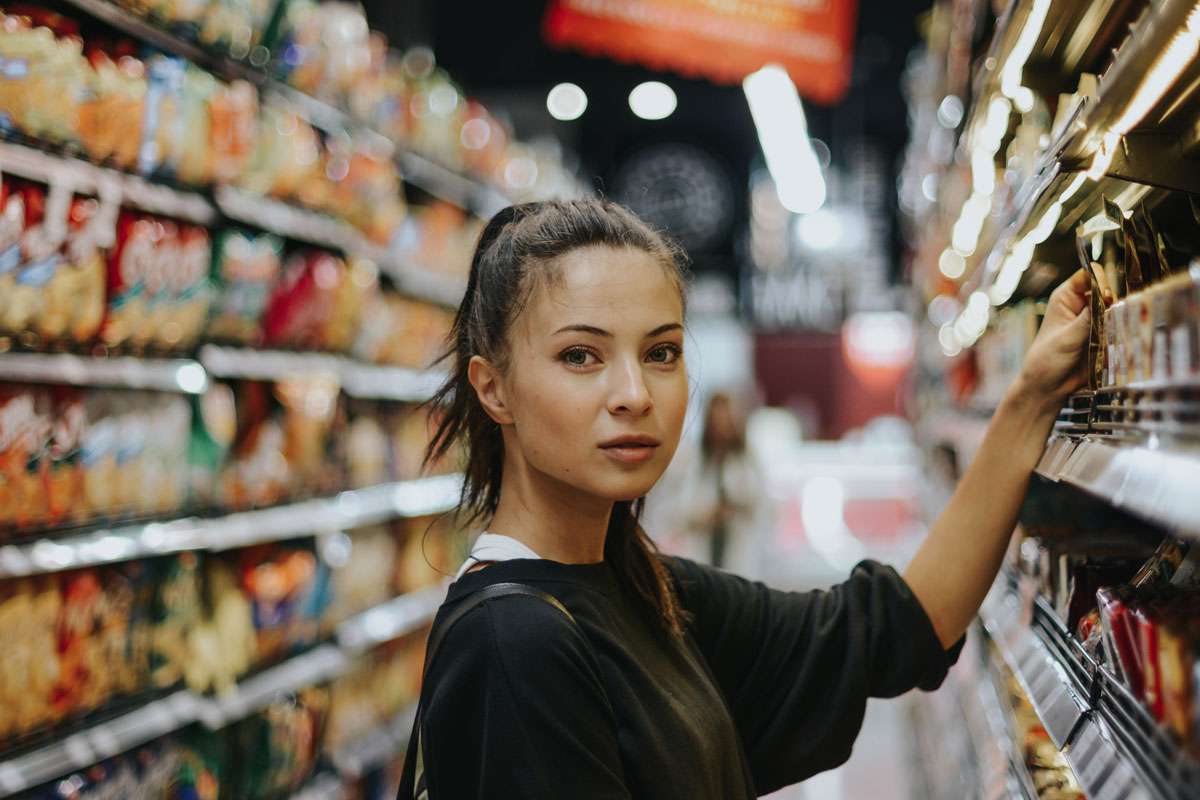 Donna giovane fa la spesa in supermercato, scelta prodotti sugli scaffali, risparmio spesa intelligente, confronto prezzi