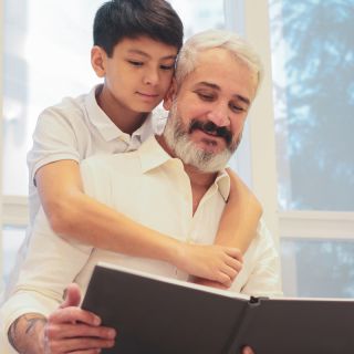 Nonno e nipote leggono insieme un libro, rappresentazione del divario digitale tra generazioni in ambiente domestico luminoso