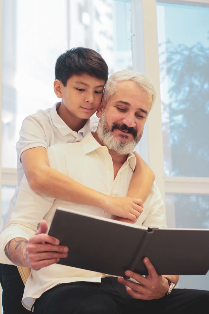 Nonno e nipote leggono insieme un libro, rappresentazione del divario digitale tra generazioni in ambiente domestico luminoso
