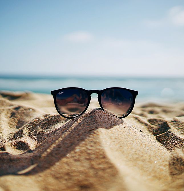 Occhiali da sole neri su sabbia dorata in spiaggia, sfondo mare e cielo estivo, concetto di caldo e risparmio energetico