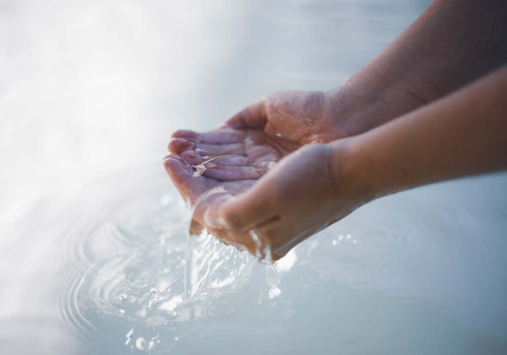 Mani che raccolgono acqua limpida, dettaglio movimento, riflessi naturali, concetto di purezza e benessere