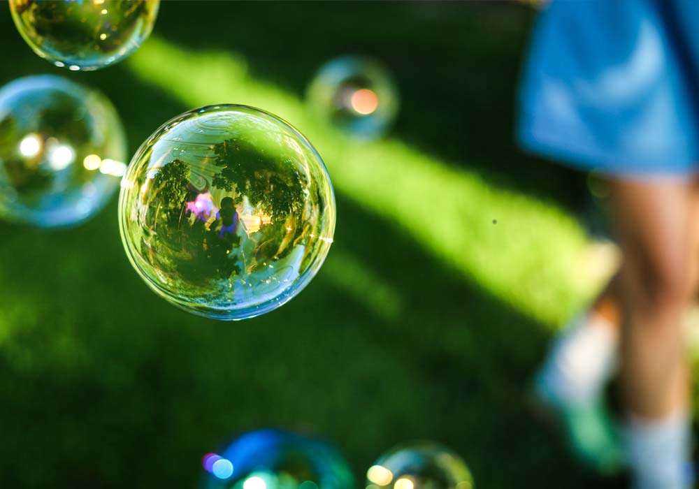 Bolle di sapone che fluttuano su prato verde, riflessi colorati, atmosfera estiva e giocosa all’aperto