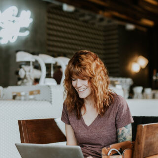 Donna sorridente lavora al laptop in un bar moderno, concetto di scelta tra tutela e mercato libero energia