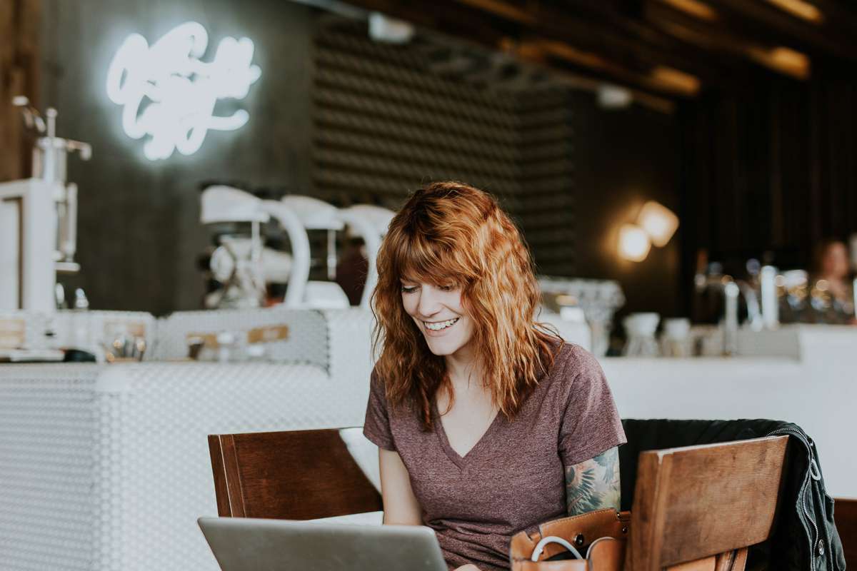 Donna sorridente lavora al laptop in un bar moderno, concetto di scelta tra tutela e mercato libero energia