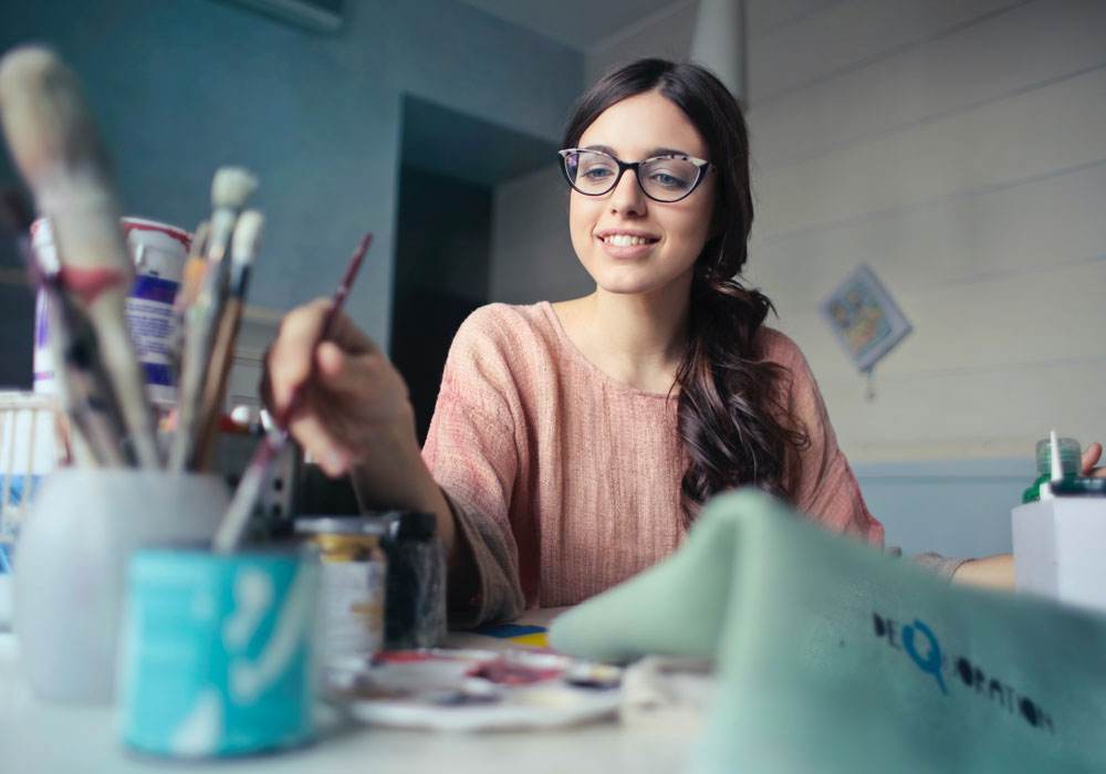 Donna sorridente dipinge in studio artistico, pennelli e colori acrilici su tavolo, ambiente creativo e protetto
