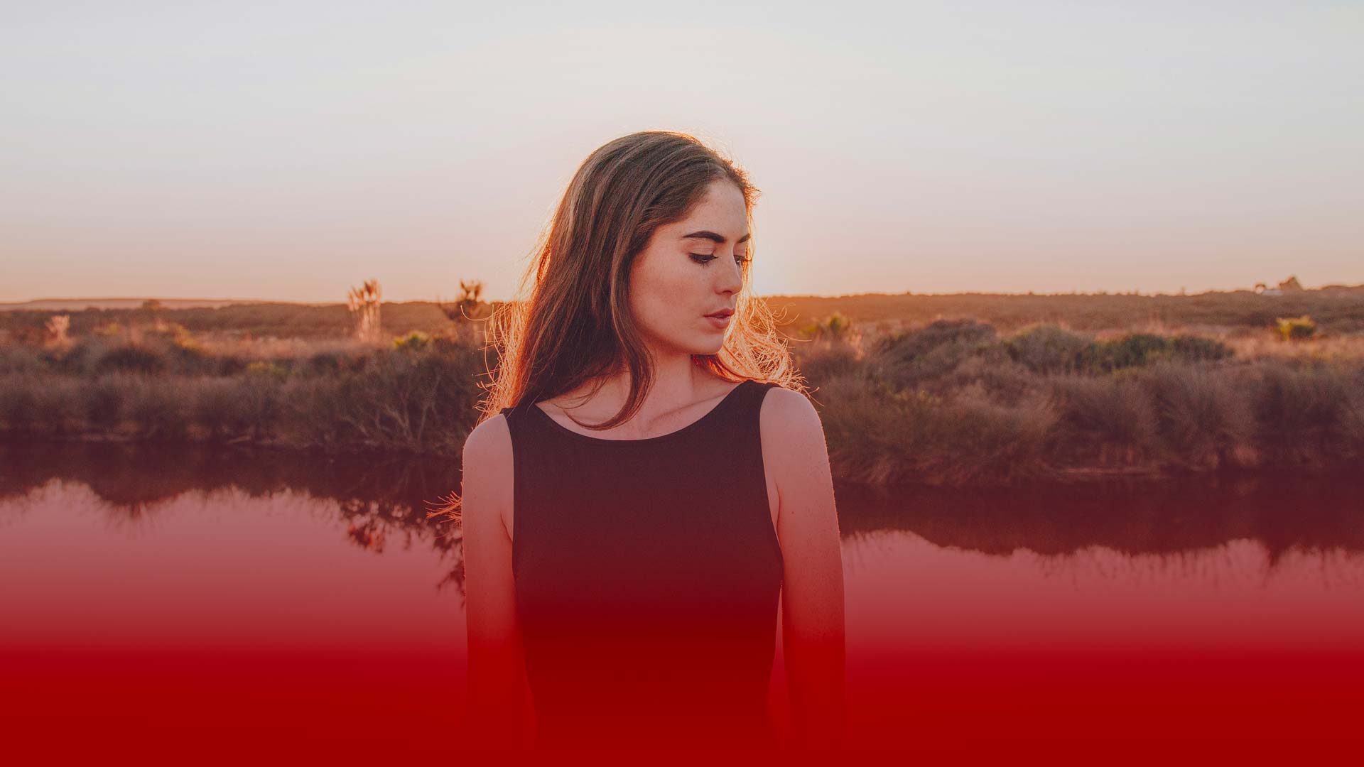 Donna con capelli castani in abito nero al tramonto, sfondo naturale, banner rosso sfumato in primo piano